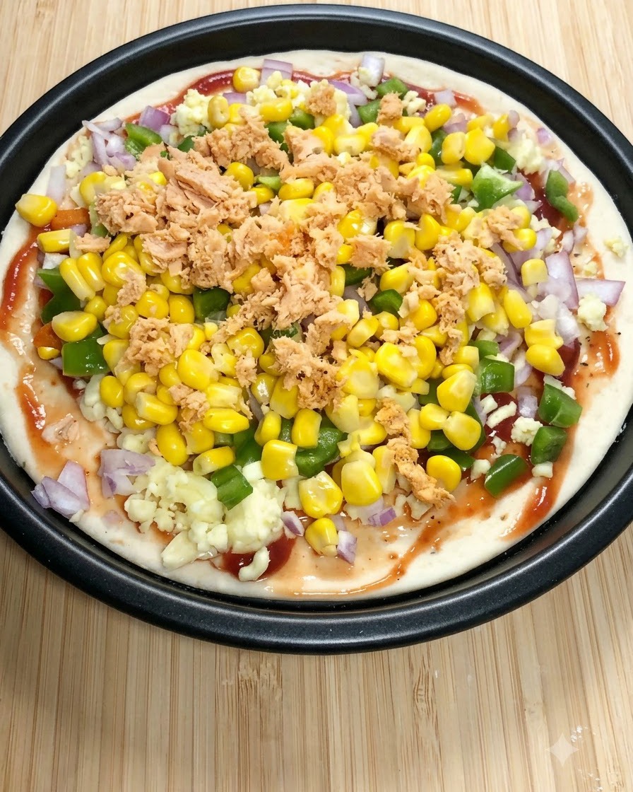 A round pizza base topped with tomato sauce, mozzarella, green bell peppers, sweet corn, and flaked canned salmon.