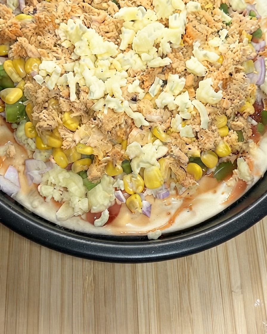 A close-up view of a prepared pizza being heavily topped with a thick layer of shredded mozzarella cheese.