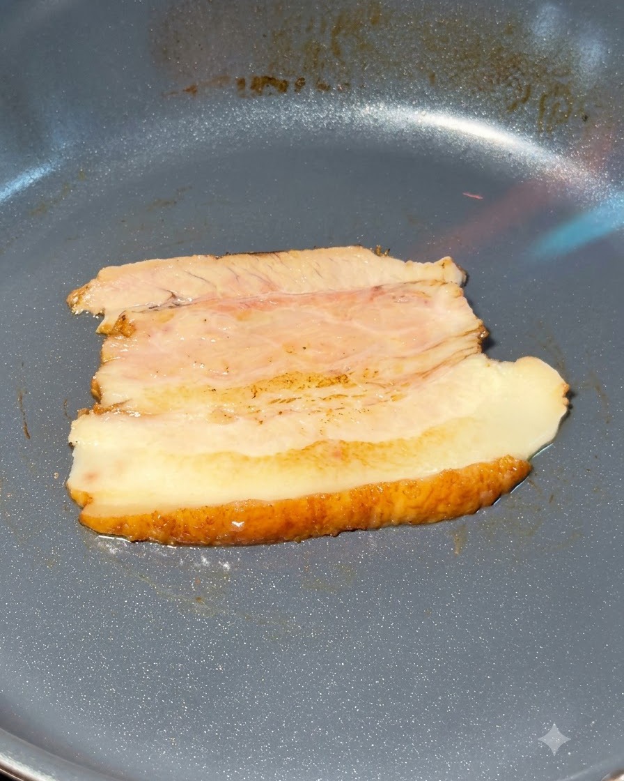 Chashu pork belly slices being torched in a frying pan.