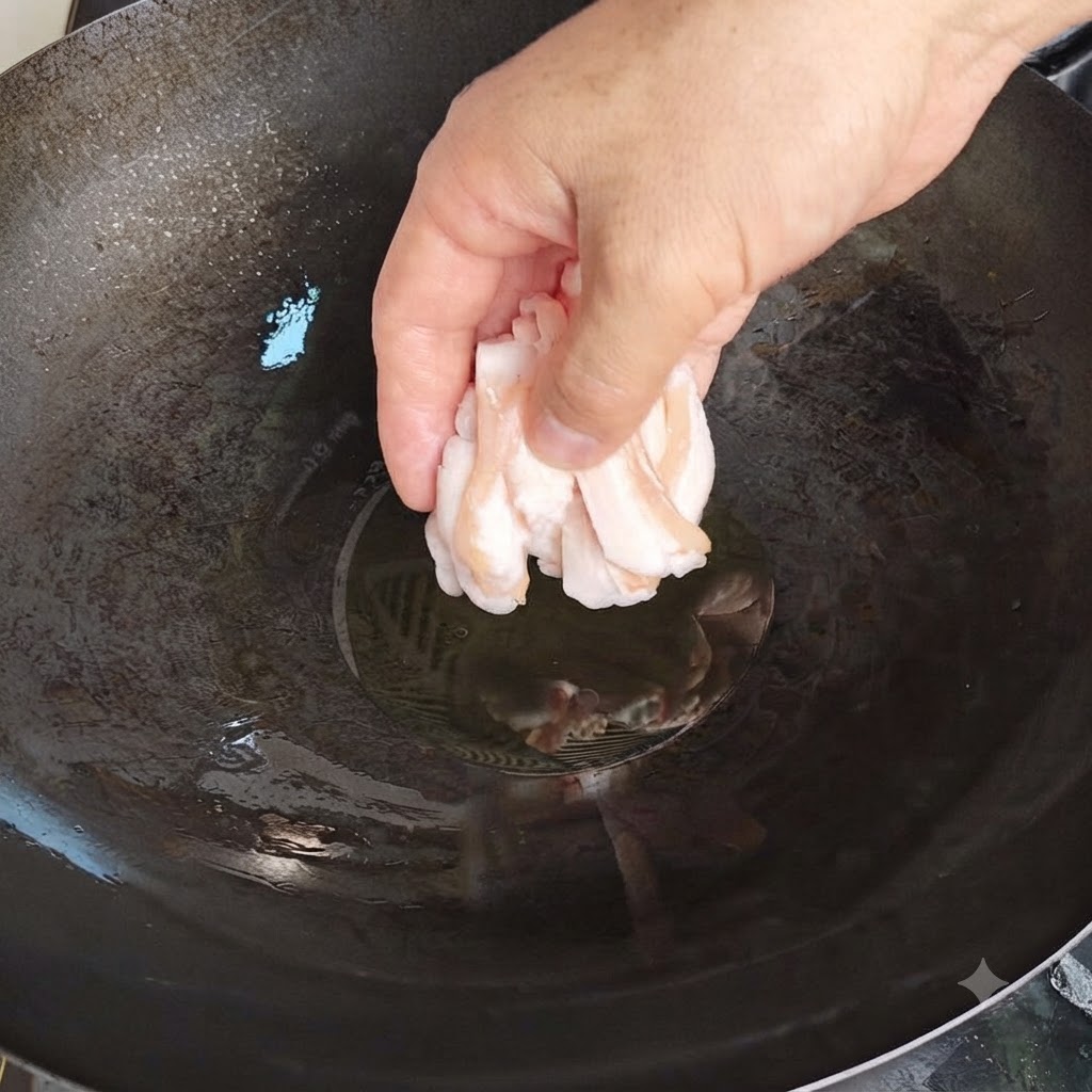 A hand carefully dropping thin slices of raw pork fat into a hot wok with oil.