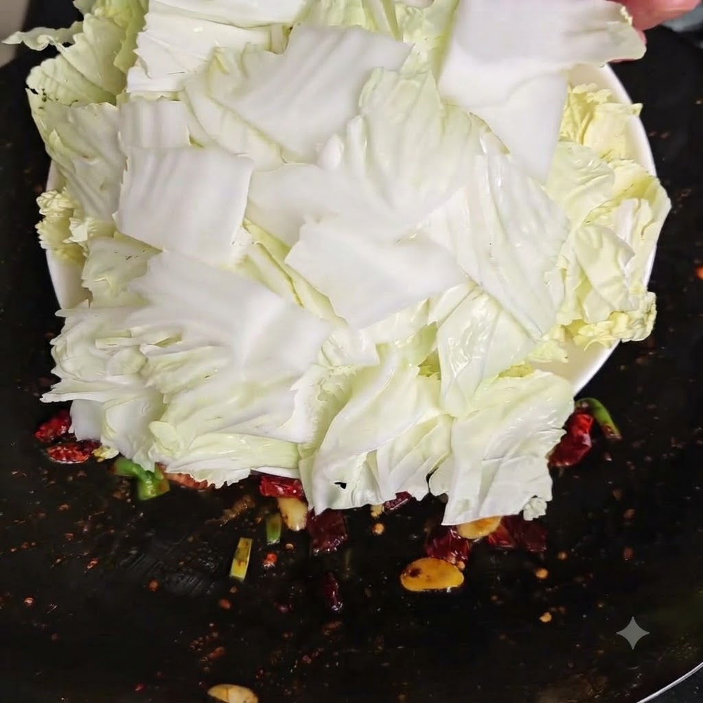 Freshly chopped raw Chinese cabbage pieces being tipped from a white plate into a hot wok.