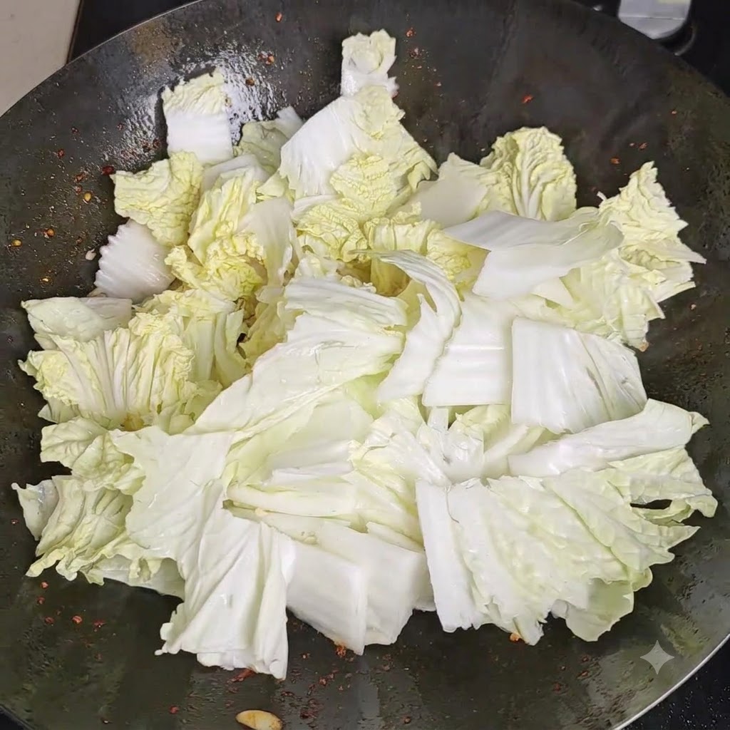 Salt being evenly sprinkled over a mound of fresh Chinese cabbage pieces inside a wok.