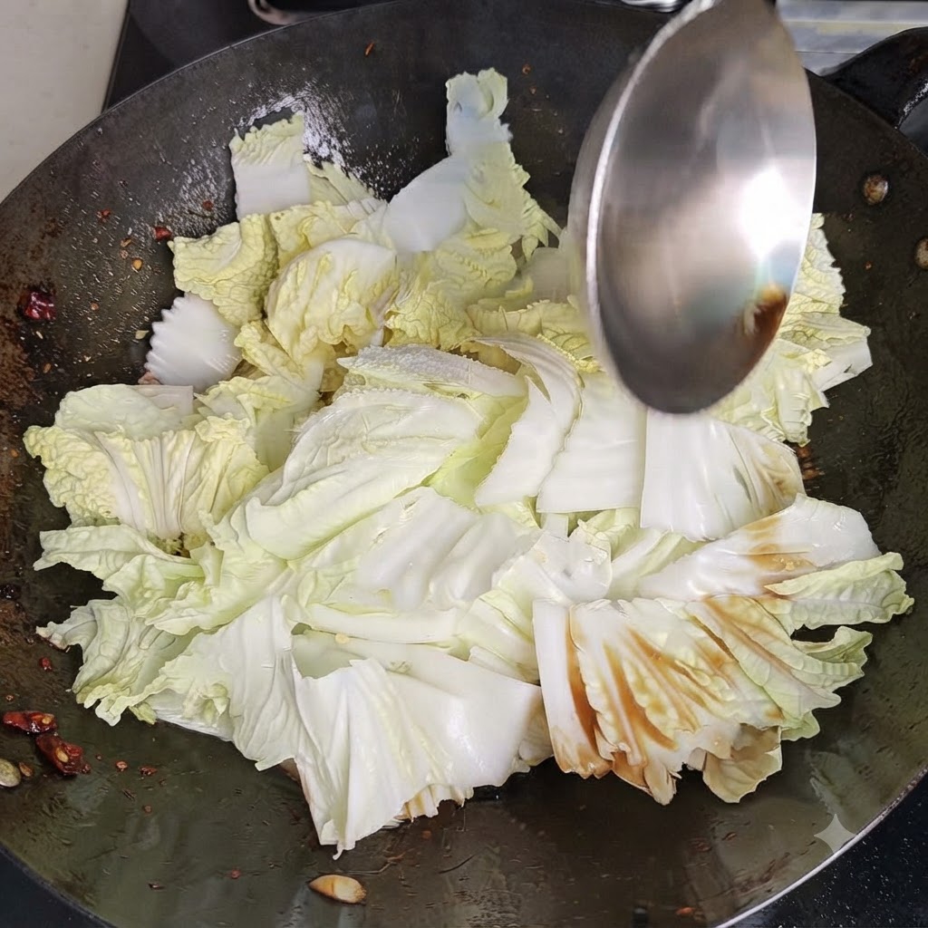 A metal wok spatula tossing and stirring Chinese cabbage and seasonings vigorously inside a hot wok.