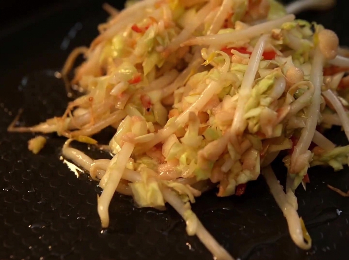 A heap of mixed shredded cabbage and bean sprouts sizzling on a black hot plate.