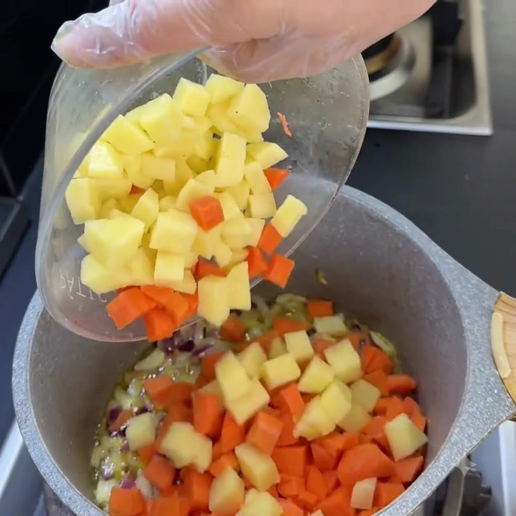 Diced carrots and potatoes sliding from a clear bowl into the cooking pot.