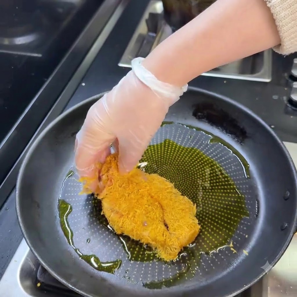 A breaded pork cutlet frying in a pan of hot oil until golden brown.