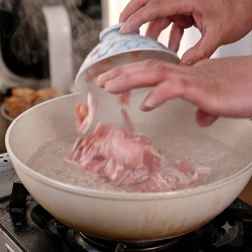 Hands dropping sliced raw pork belly from a small ceramic bowl into a pan of actively boiling water.