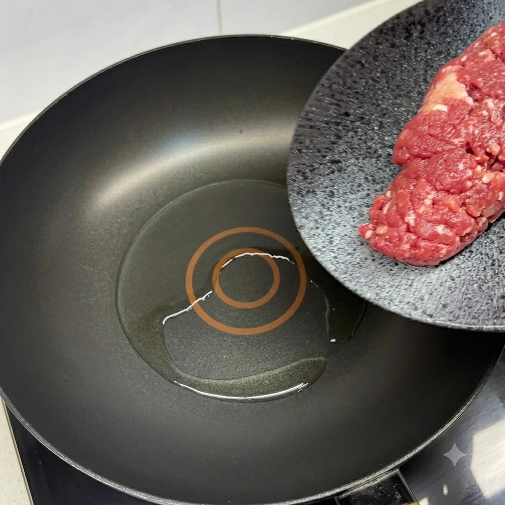 Fresh minced beef being added to a hot oiled black pan with a red spatula.
