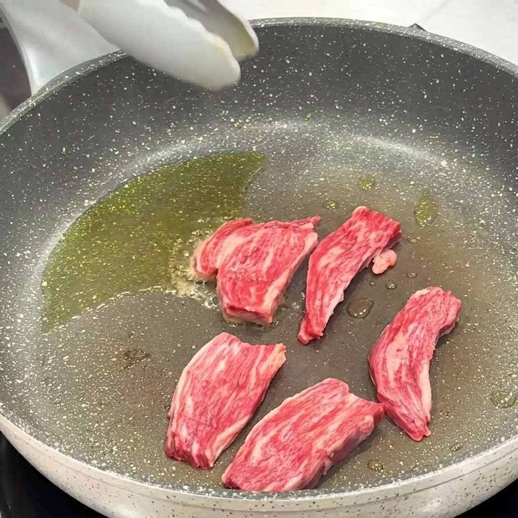Salt and black pepper being seasoned onto steak pieces cooking in the pan.