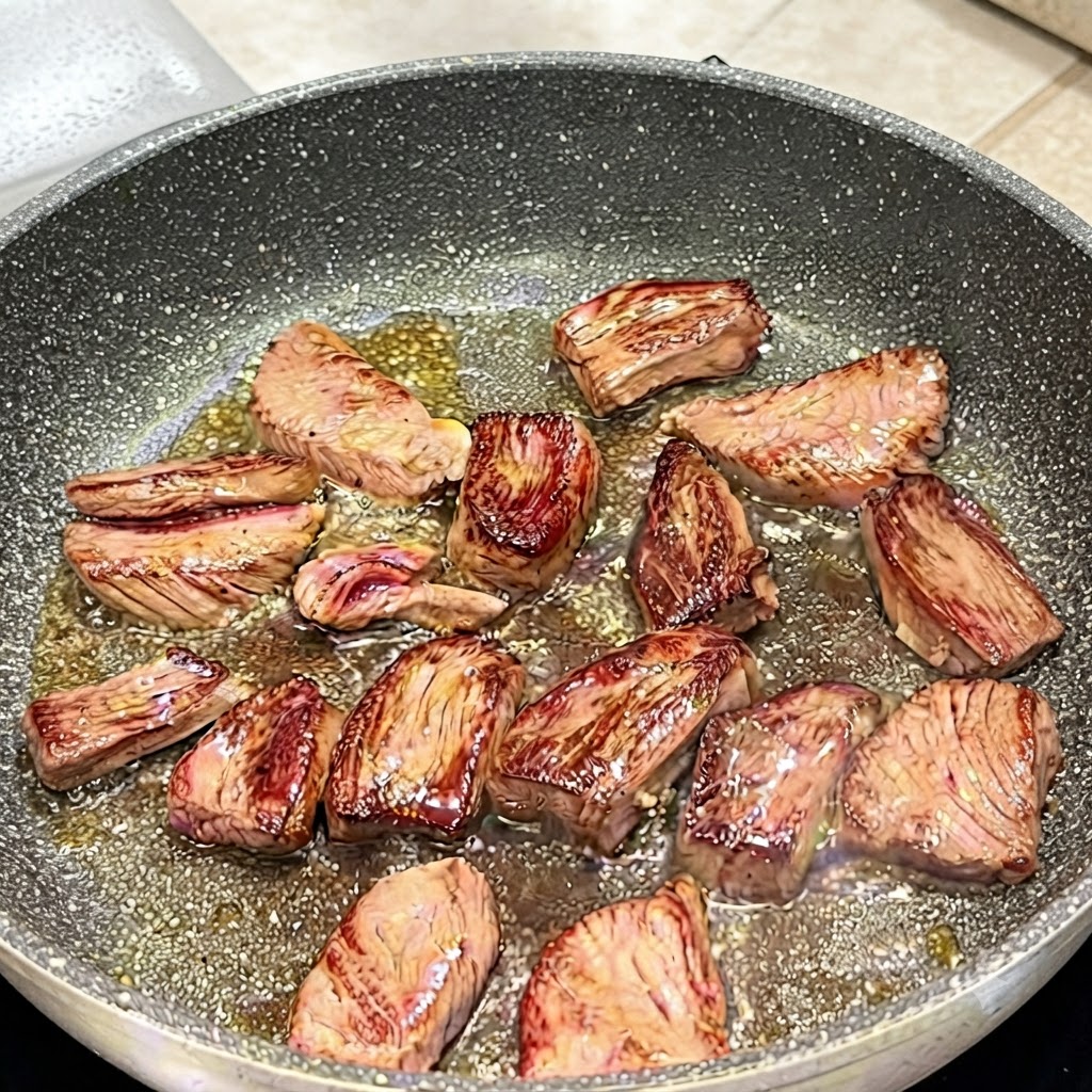 Tongs flipping skirt steak pieces in a pan to show browned surfaces.