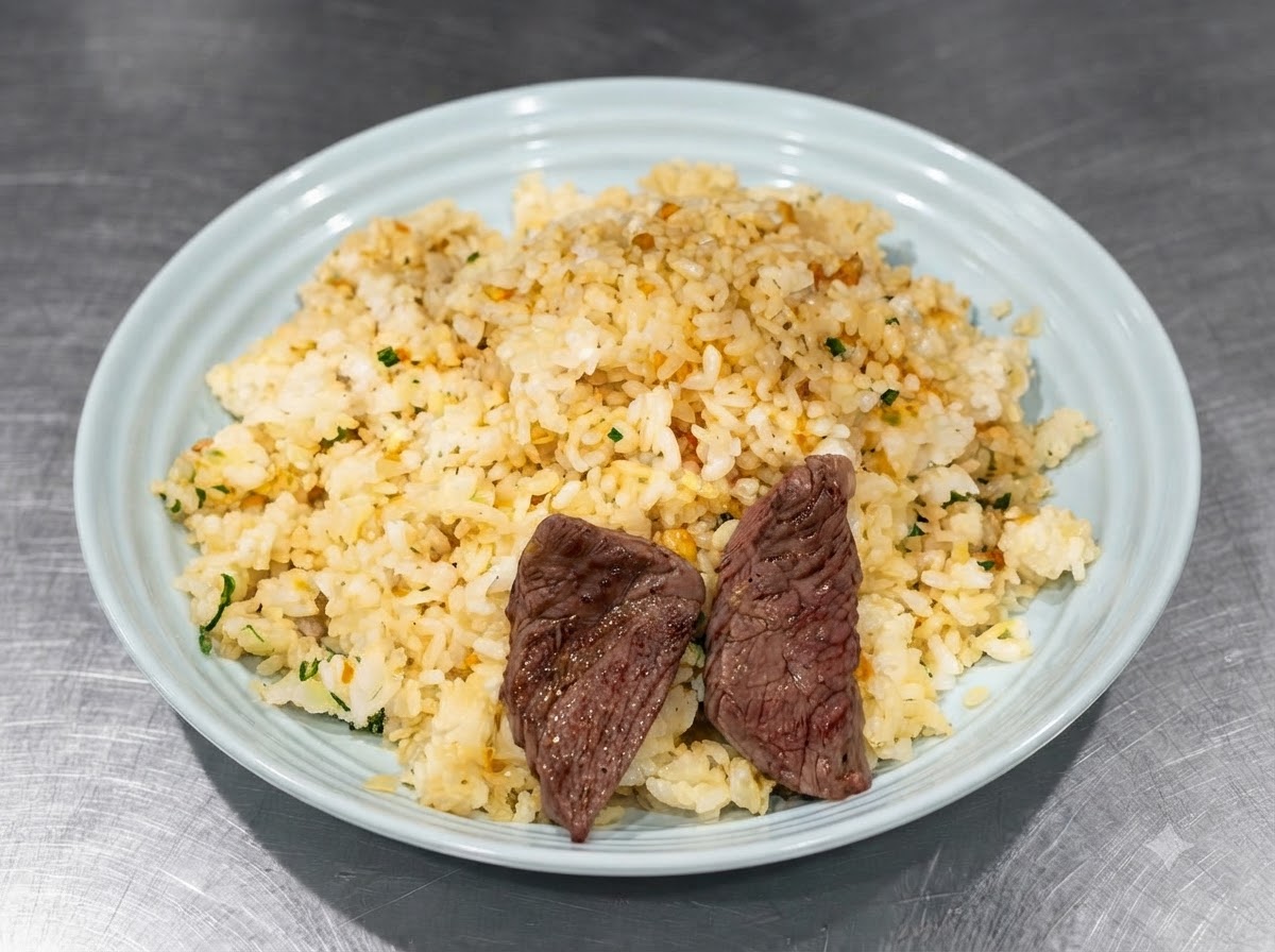Seared steak pieces being arranged on top of the seasoned rice in a blue plate using tongs