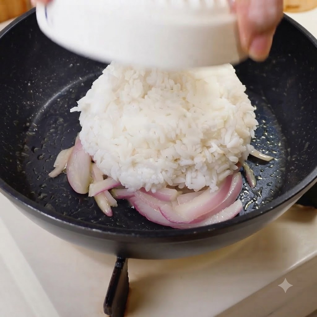 A molded dome of white rice being inverted into the center of a pan with onions.