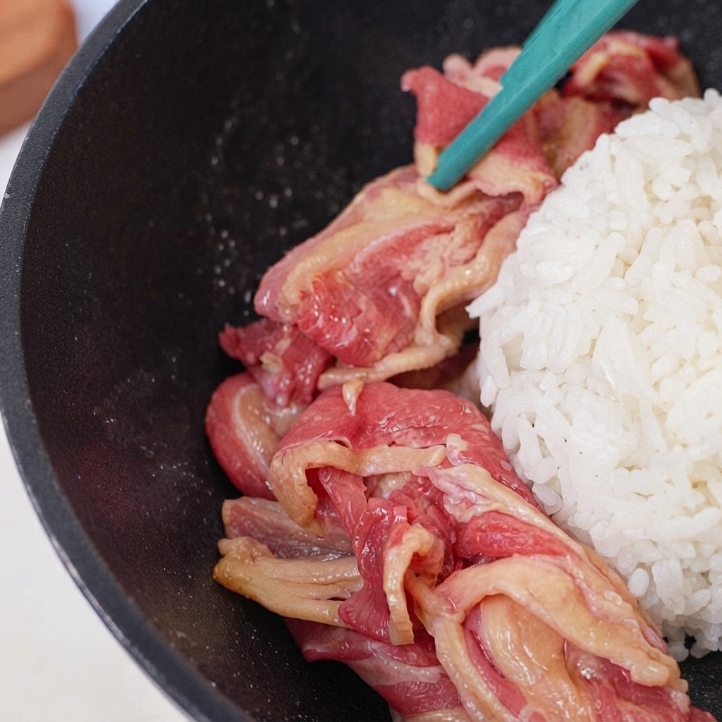 Raw beef slices placed in a ring around the mound of rice inside the skillet.