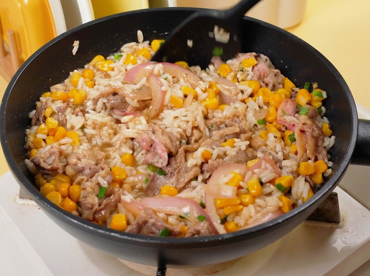 A black spatula mixing rice, beef, corn, and onions together in a pan over heat.