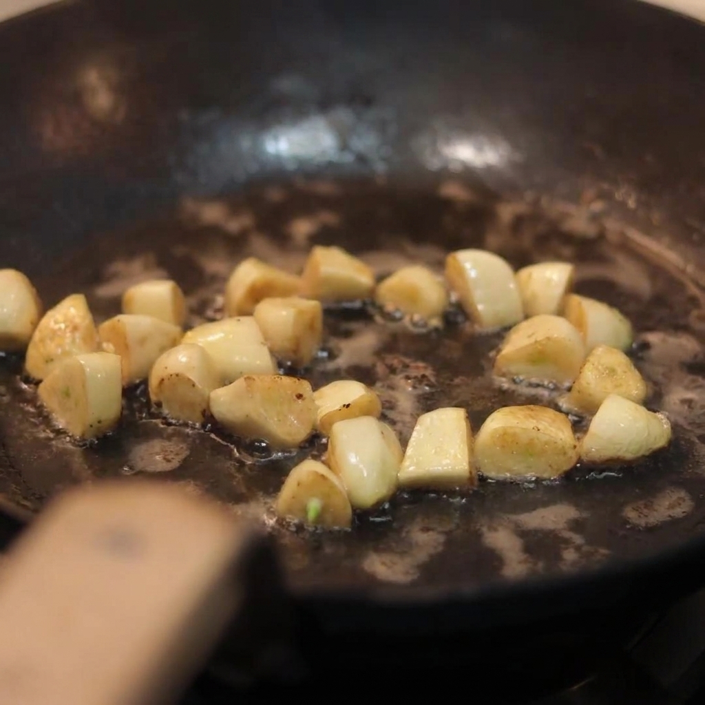 Sliced white mushrooms being tossed into a skillet containing golden sautéed garlic cloves.