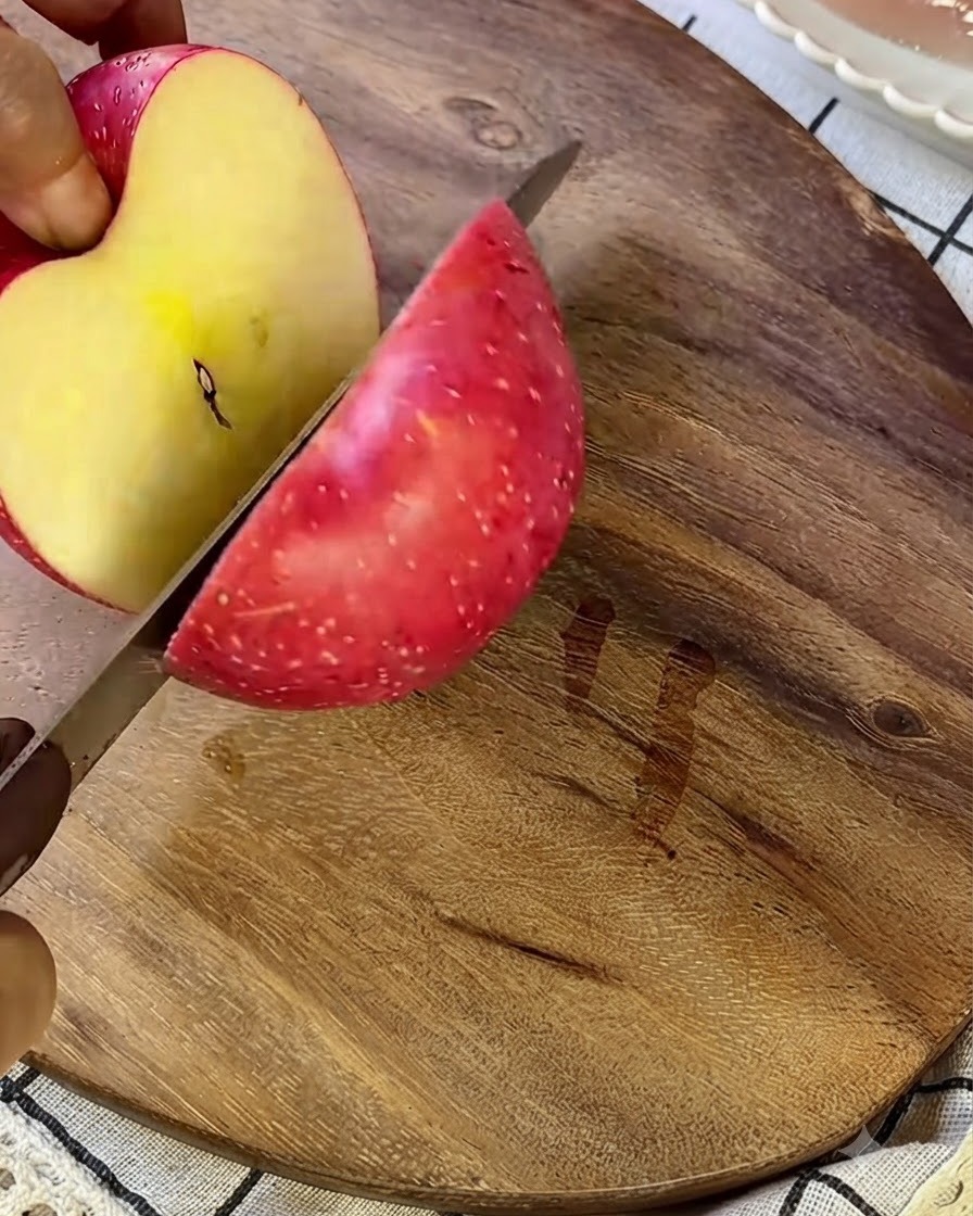 An apple being cut into small pieces on a wooden cutting board with a silver knife.