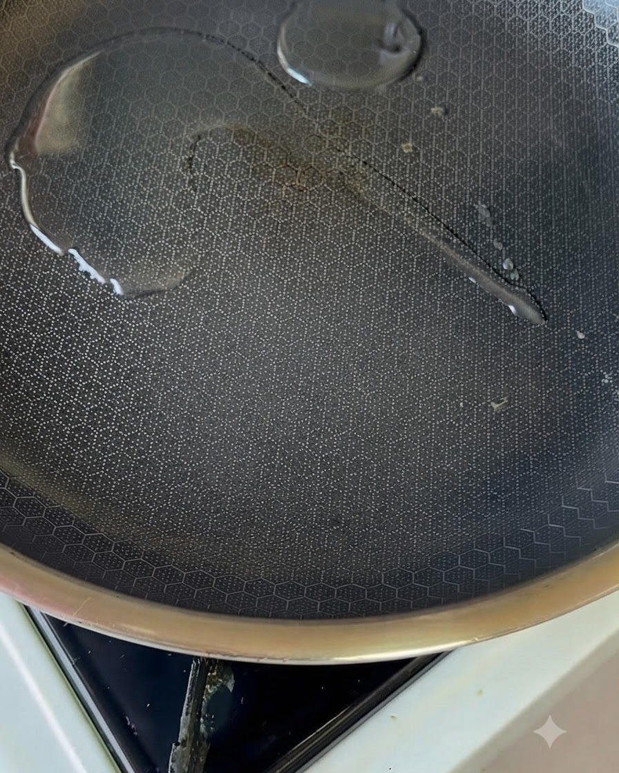 A small pool of oil glistening inside a heated non-stick pan on a stovetop burner.
