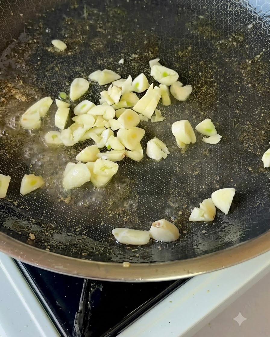 Slices of fresh garlic gently frying in cooking oil inside a non-stick pan.