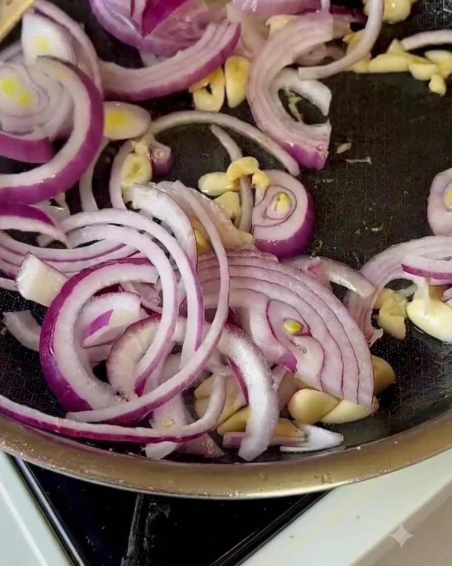 Sliced red onions, garlic, and apple chunks being tossed in a frying pan.