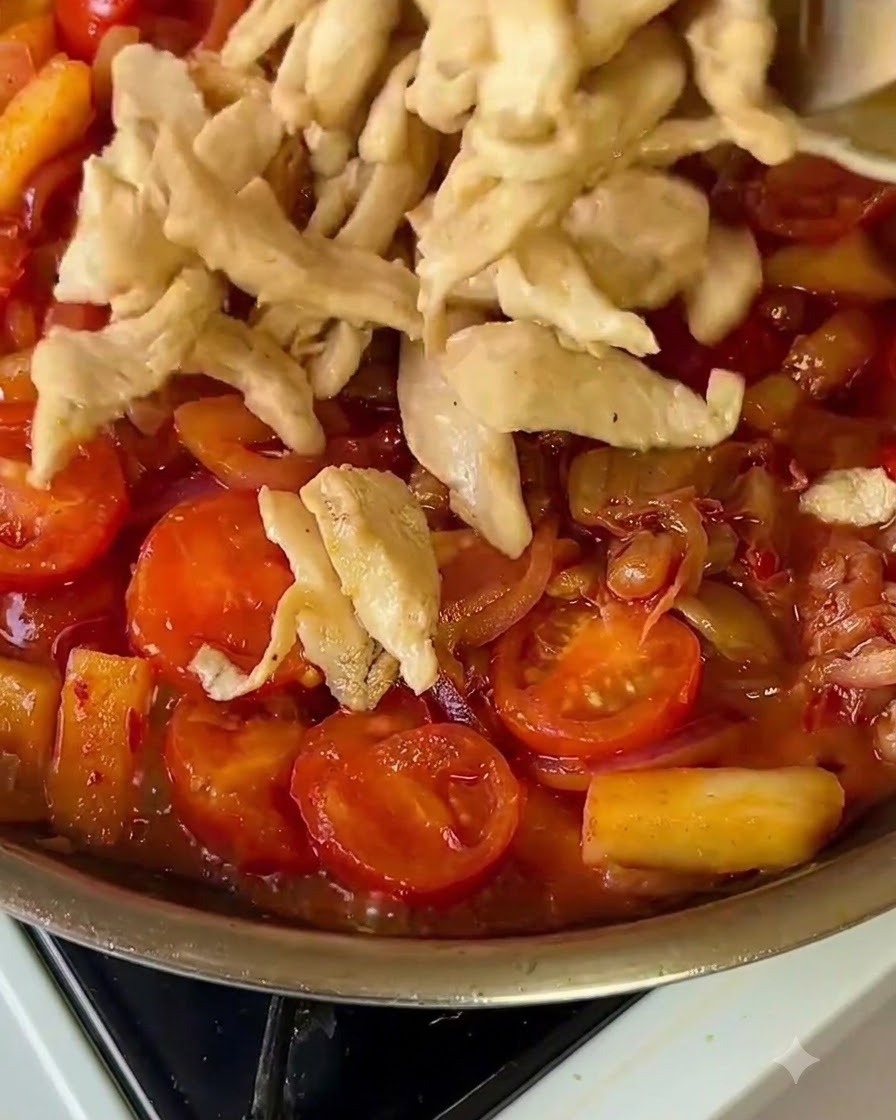 Cooked chicken strips being added back into a vibrant pan of vegetables.