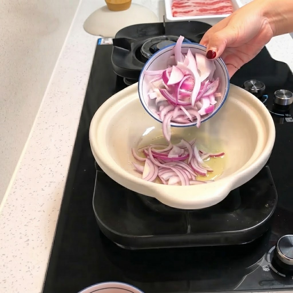 Red onion slices and peeled tomato pieces being poured from a small bowl into a hot clay pot with oil.