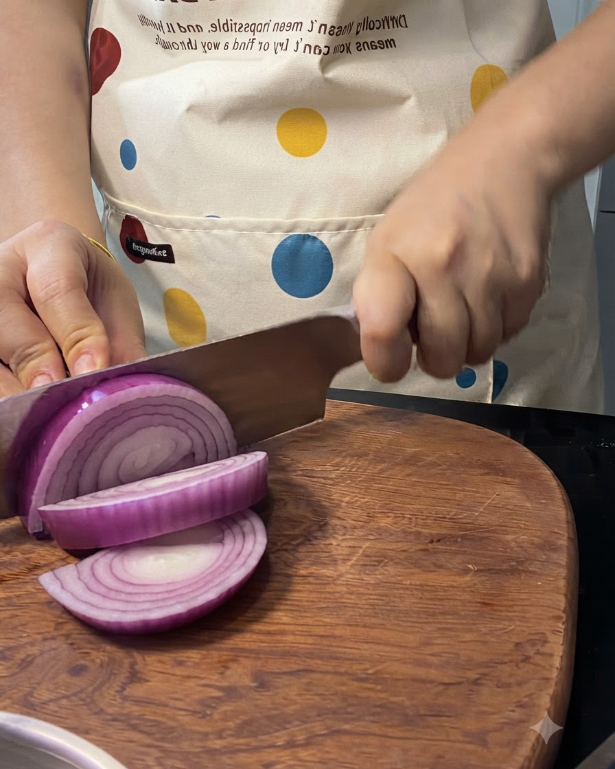 A red onion being sliced on a wooden board with a knife.