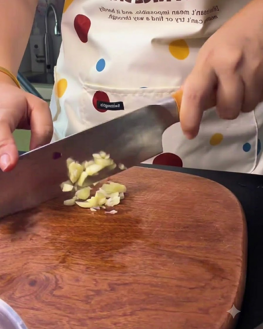 Garlic cloves being chopped and minced with a kitchen knife on a wooden board.