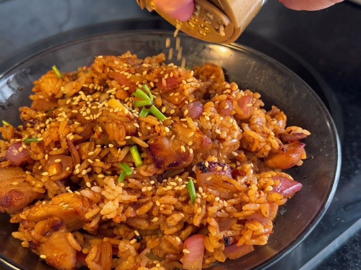 Kimchi being added to the pan and stir-fried together with the chicken and onions.