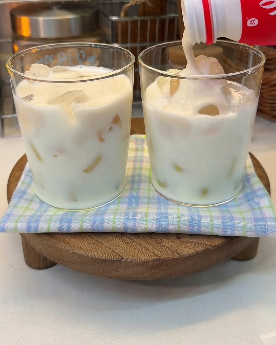 Thick yogurt being poured from a bottle into a glass of iced milk.