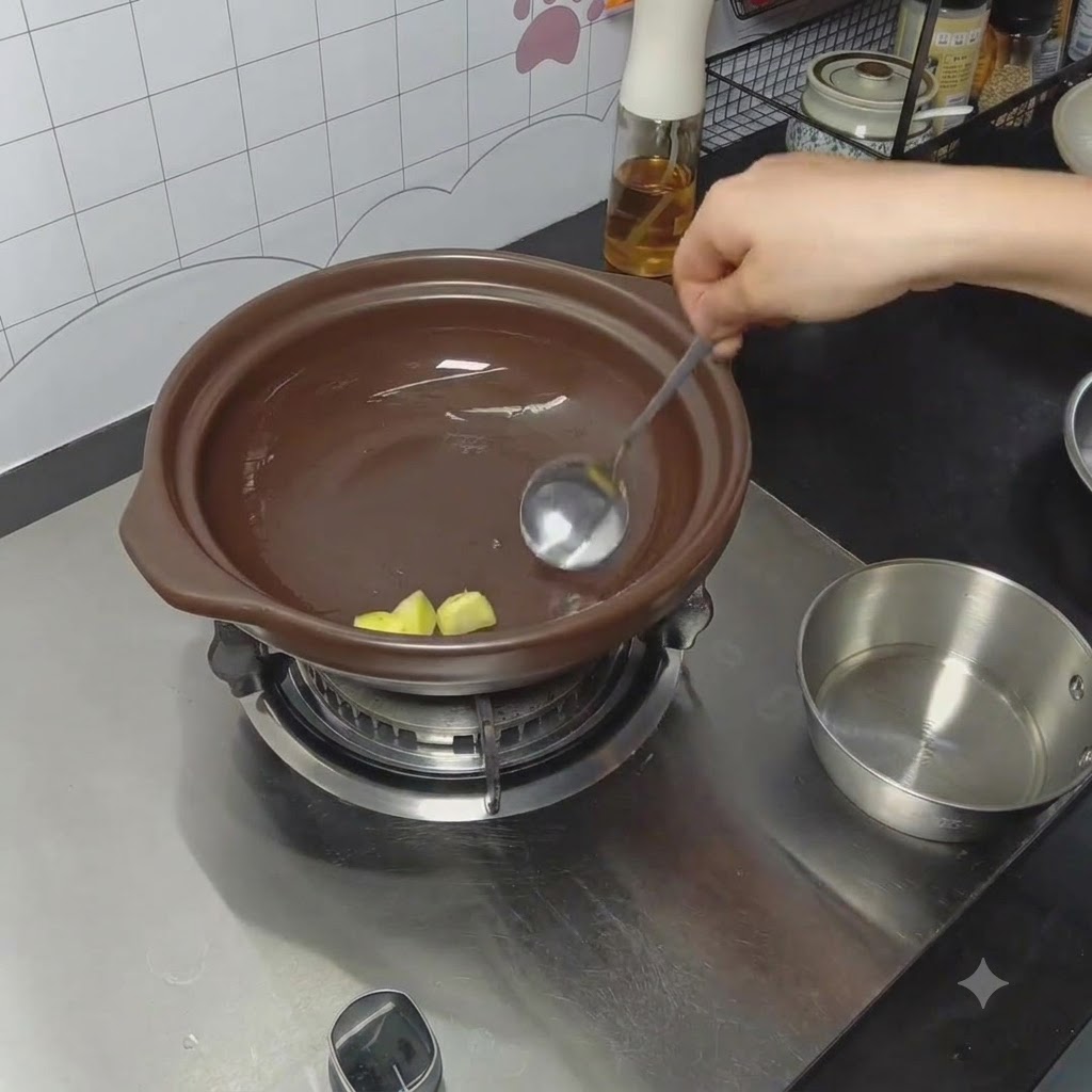 Ginger being rubbed with oil at the bottom of a clay pot using a spoon.