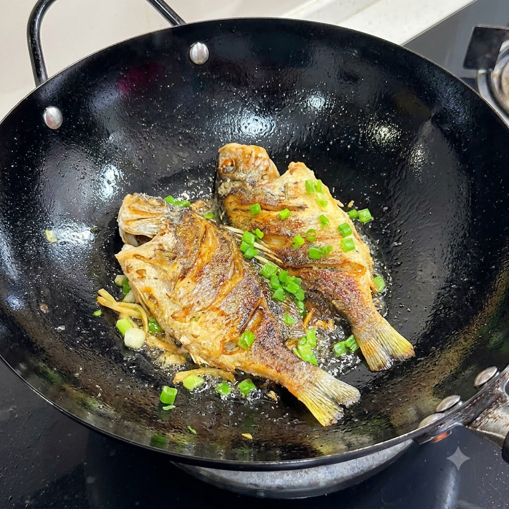 Chopped green onions being sprinkled on top of golden pan-fried fish in a black wok.