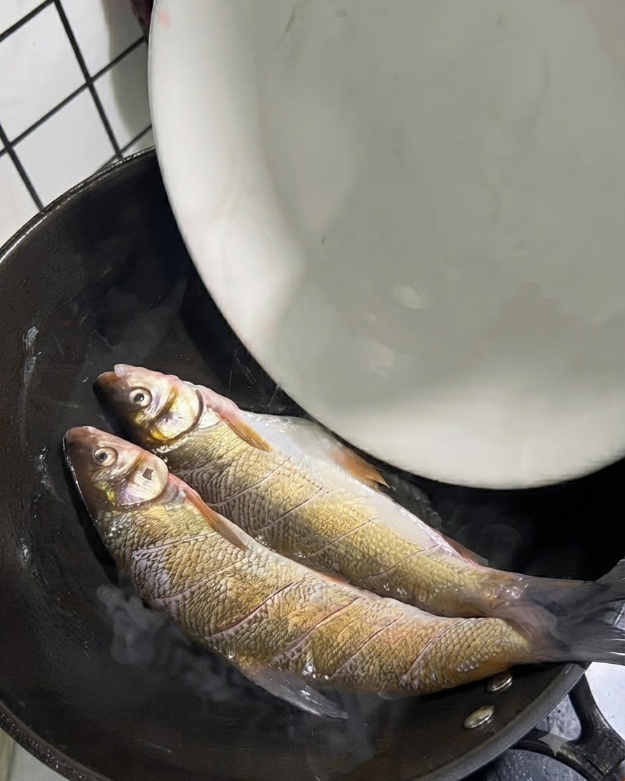 Two whole yellow tail fish placed inside a hot wok with oil.