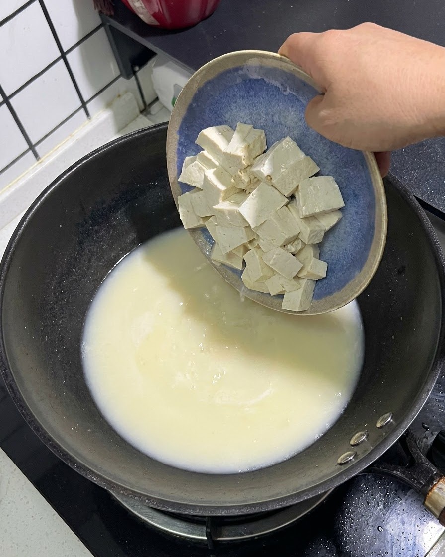 White tofu cubes sliding from a blue plate into a pot of creamy white fish broth.
