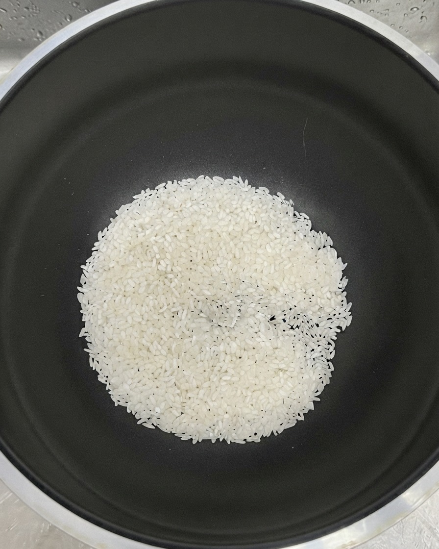 White rice gathered at the bottom of a black pot with water added for rinsing.