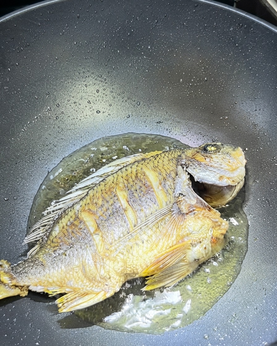 Sliced ginger and garlic scattered around the fried fish in a wok.