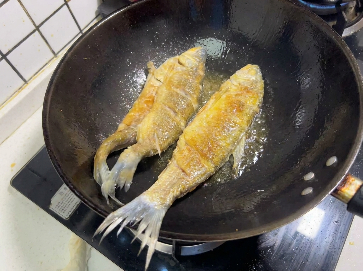 Two whole fish frying in hot oil in a wok, showing a crispy golden-brown crust.