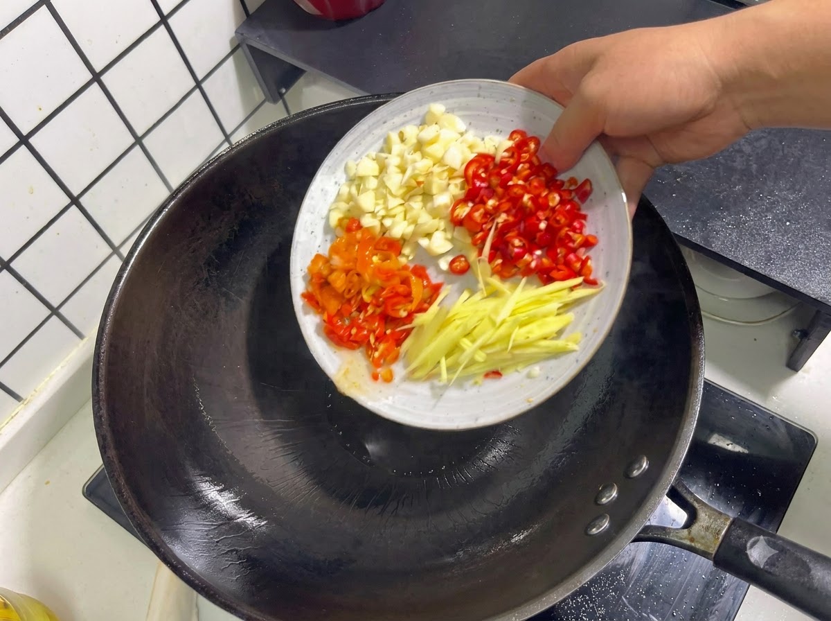 Minced garlic, red chili peppers, pickled peppers, and ginger strips being tossed into a wok.