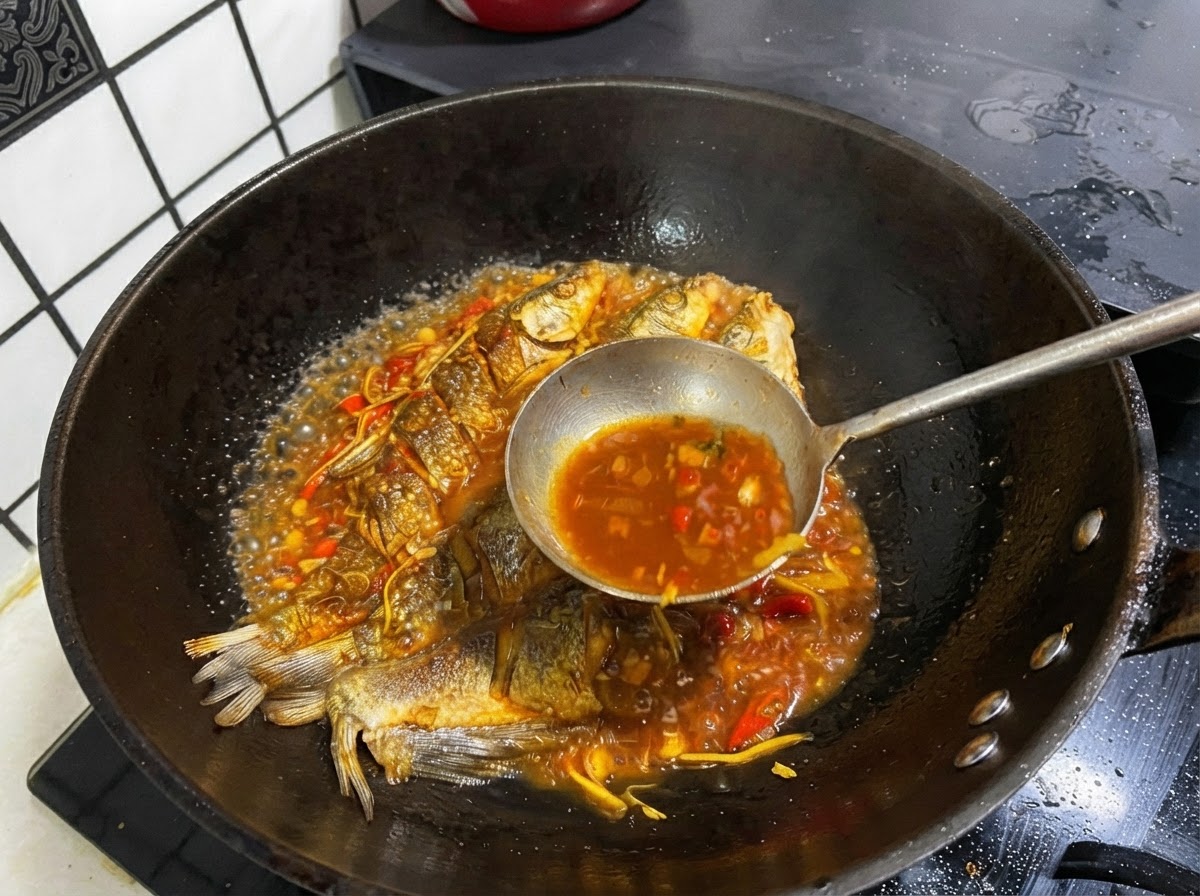 A metal ladle scooping dark savory broth from a pan containing whole fried fish.