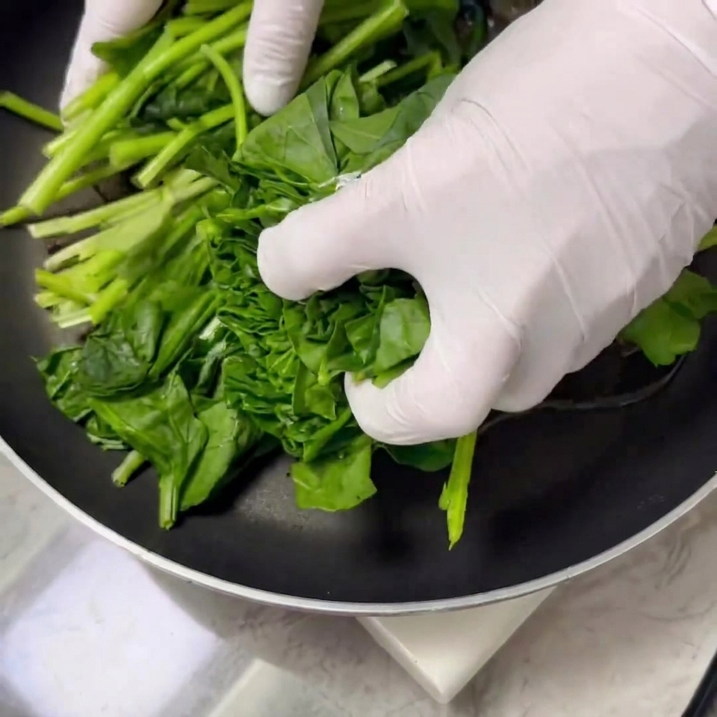 Fresh spinach leaves being tossed and cooked in a skillet with oil and salt.