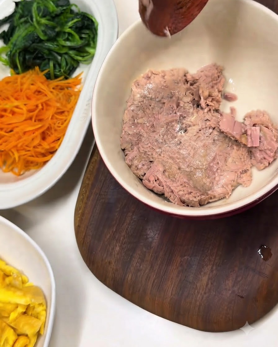 A bowl of flaked canned tuna next to a white platter with prepared spinach and carrots.