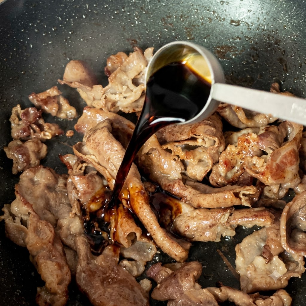 A measuring spoon pouring dark light soy sauce over cooked beef slices in a pan.