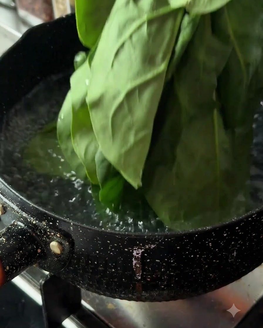 Fresh spinach leaves being lowered into a pot of boiling water on a stove.