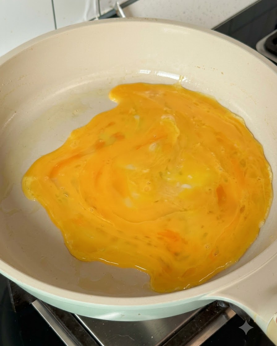 Beaten eggs spreading across the hot pan to form an egg pancake.