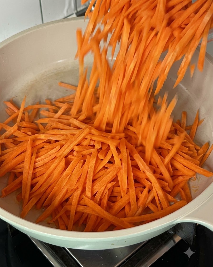 Fresh shredded carrots being tossed and stir-fried in a hot pan.
