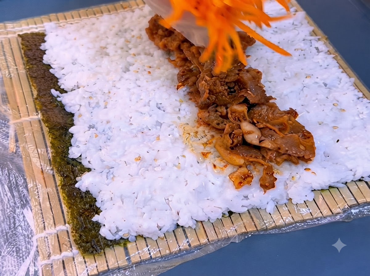 Shredded carrots being placed over a strip of seasoned grilled beef on top of white rice.