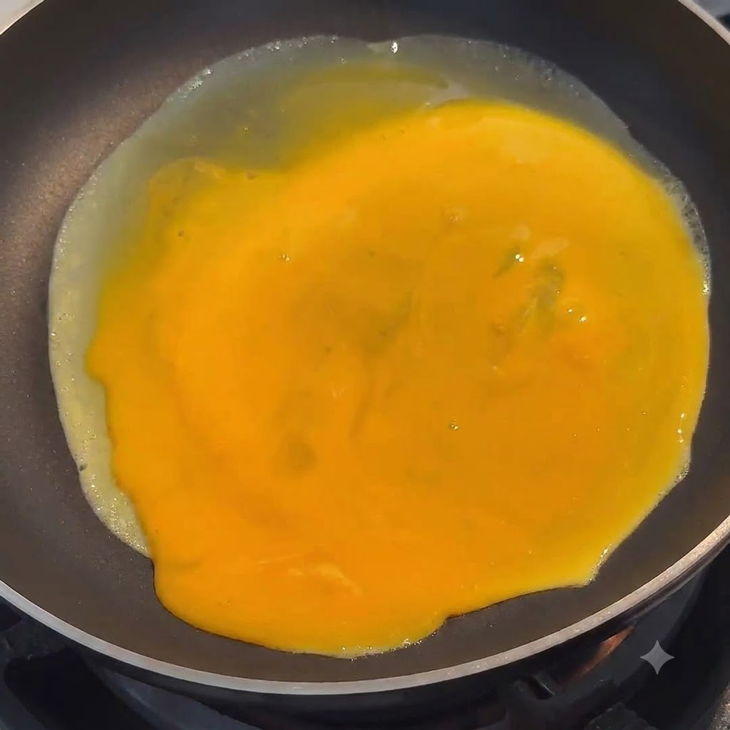 Vibrant yellow beaten egg spreading evenly across the surface of a black skillet.