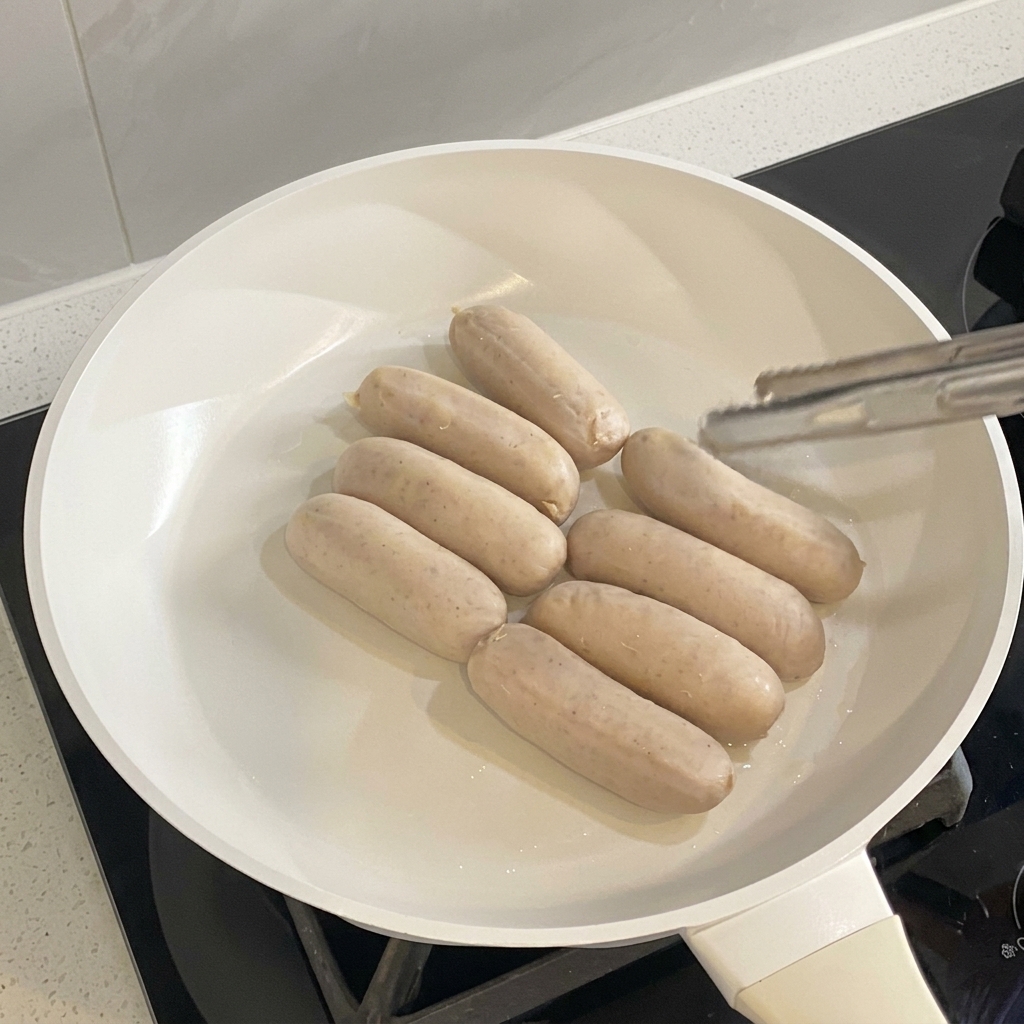 Sausages cooking and browning evenly in a white skillet.