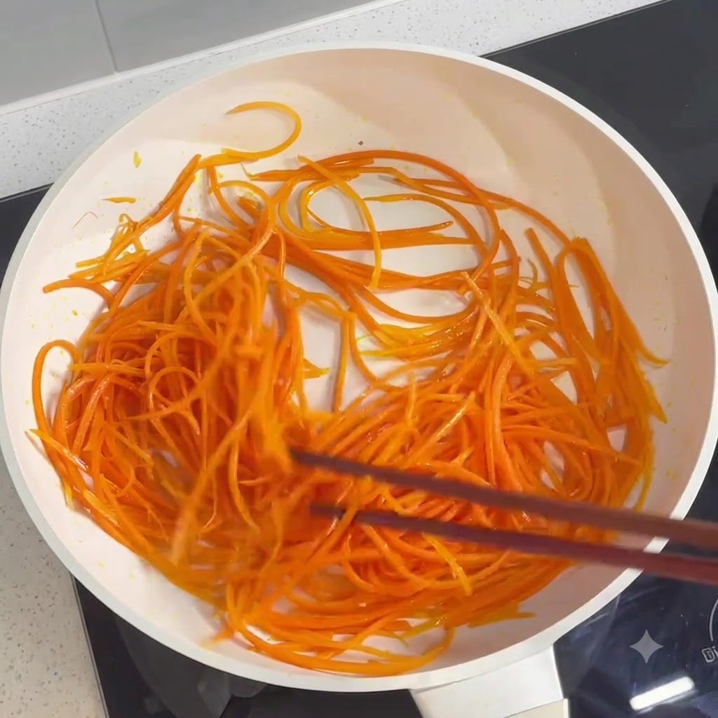 Shredded carrots being tossed and cooked in a pan using chopsticks.