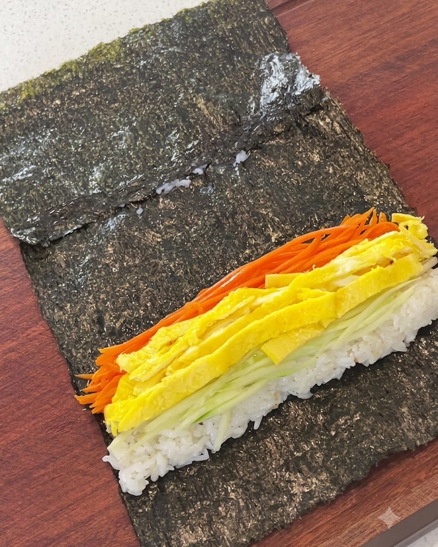 Shredded carrots, egg strips, cucumber, and fish cake arranged over rice on a sheet of seaweed.