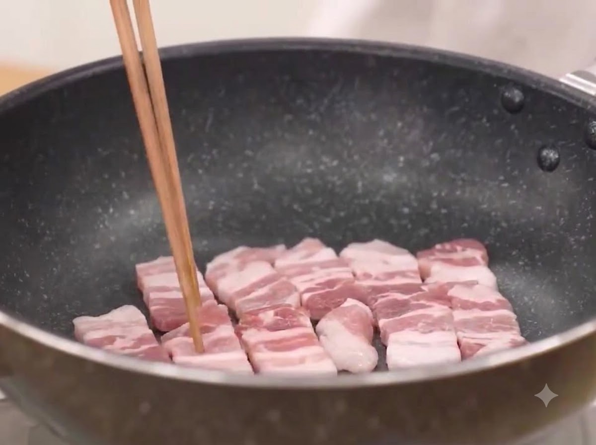 Pork belly slices being fried in a hot pan until sizzling.